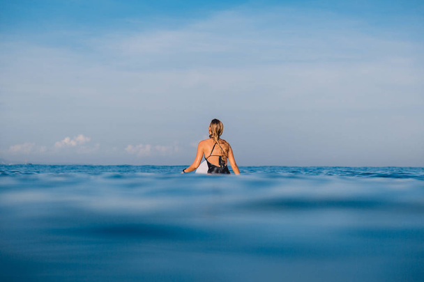 Rückansicht einer Surferin, die auf einem Surfbrett im Ozean sitzt, mit Insel im Hintergrund  - Foto, Bild