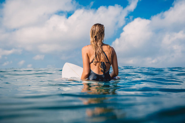серфер женщина сидит на доске для серфинга в океане с острова на заднем плане
  - Фото, изображение