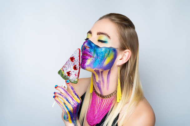New make-up universe is painted on womans face. Forehead brows eyes are chic evening make-up green color, wavy line divides the face into two parts. At the bottom of her face are streams vivid paint - 写真・画像