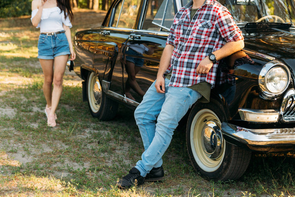 a man in jeans and a red shirt in a cage is facing a vintage, retro car, waiting for the girl,looking at the sunset and waiting for a woman - Foto, Imagen