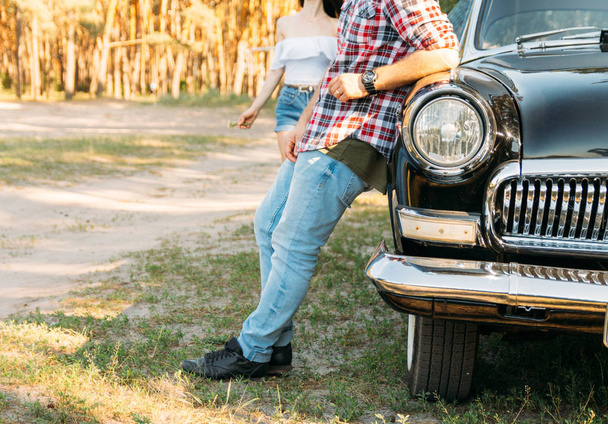 un homme en jean et une chemise rouge dans une cage fait face à une voiture vintage et rétro, attendant la fille, regardant le coucher du soleil et attendant une femme
 - Photo, image