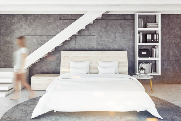 Woman in Scandinavian style bedroom interior with concrete walls and floor with a carpet, stairs, and a white double bed with a bookcase. 3d rendering toned image blurred - Foto, afbeelding