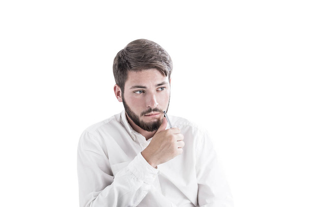 Troubled young bearded caucasian businessman wearing a white shirt sitting with pen near his face and thinking looking sideways. Concept of work and life troubles and decision making Isolated portrait - Фото, изображение