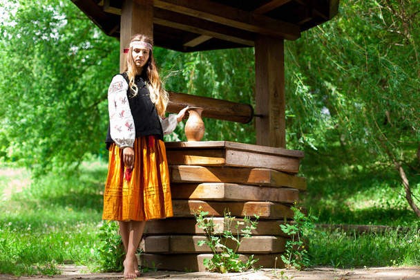 Beautiful Ukrainian woman is wearing embroidery near a wooden well - Fotoğraf, Görsel