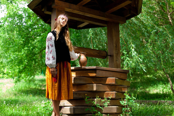 Beautiful Ukrainian woman is wearing embroidery near a wooden well - Fotografie, Obrázek