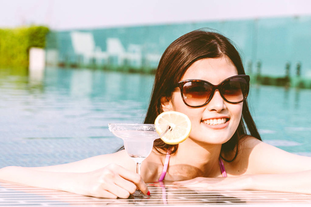 Женщина в бикини выпивает коктейль в бассейне во время летнего отдыха в курортном спа
 - Фото, изображение