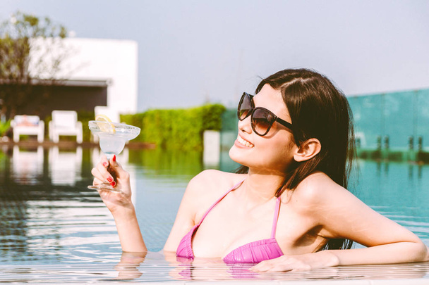 Mulher vestindo biquíni bebendo coquetel na piscina nas férias de verão relaxante no resort spa
 - Foto, Imagem