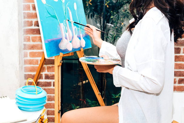 Young woman artist drawing on canvas with color palette and watercolor paints at home - 写真・画像