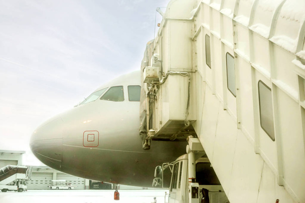Γέφυρα closeup jet και λευκό αεροπλάνο σταθμευμένο στο αεροδρόμιο το έδαφος και το χειμώνα φόντο μπλε του ουρανού. - Φωτογραφία, εικόνα