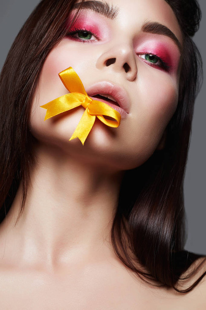 Sensual Beautiful Girl with makeup and silk bow on lips. beauty make-up girl with pink eye shadow. young Woman - 写真・画像