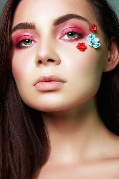 顔に花を持つ美しい少女。ピンクのアイシャドウと美容メイクアップ女性 - 写真・画像