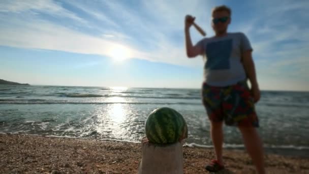 slow motion: a young sexy guy beats a baseball bat with vegetables and a watermelon fruit. It is located on the beach, sandy beach - Footage, Video