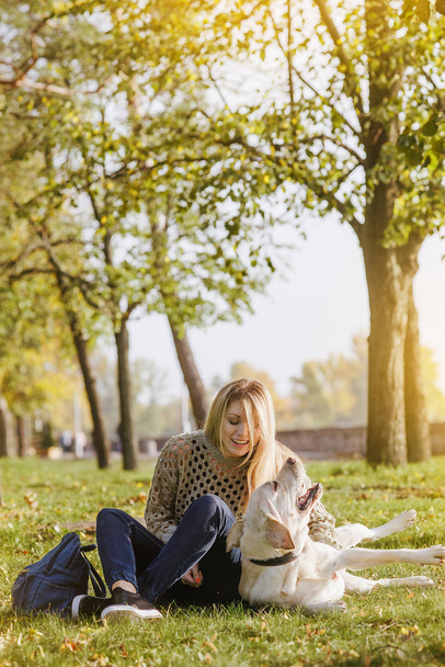 belle blonde est assise sur l'herbe dans le parc et joue avec son chien labrador
 - Photo, image
