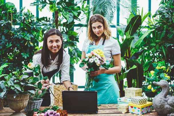 Portrait of professional colleagues collaborating creating floral composition for sale checking mail on laptop,female employee assist owner of flower shop composing bouquet completing client orde - Fotografie, Obrázek