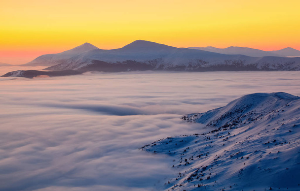 The landscape with a stunning sunset, interesting thick fog and mountains covered with textured snow on a winter day. Fantastic winter scenery. - Fotografie, Obrázek