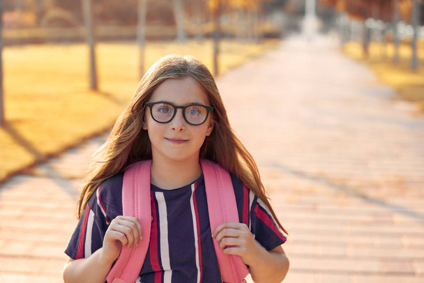 Menina estudante criança loira com óculos e mochila no parque de volta à escola
 - Foto, Imagem