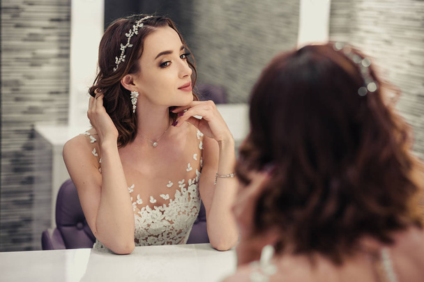 Portrait of young brunette bride woman in dressing room with wedding jewelry and dress - 写真・画像