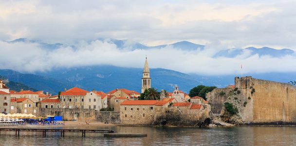 Vista a la antigua ciudad histórica de Budva en la costa del mar Adriático en Montenegro, nubes dramáticas alrededor de las montañas
. - Foto, Imagen