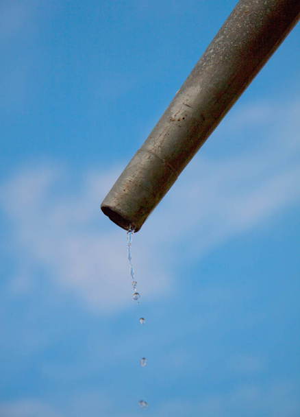 Druppels water stroomt uit pipe - close-up met blauwe lucht. Concept voor het tekort aan water- en milieuvraagstukken. Kopiëren van ruimte voor het schrijven. - Foto, afbeelding