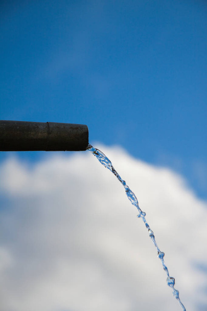Drops of water flowing from pipe - close up with blue sky. Concept for water shortage and environmental issues. Copy space for writing. - Photo, Image