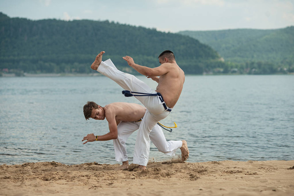 Men train capoeira on the beach - concept about people, lifestyle and sport. Training of two fighters - Φωτογραφία, εικόνα
