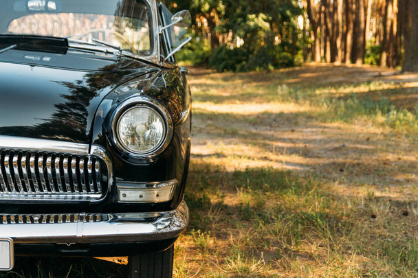 half of a black, old, vintage car with glare from the sun, which stands on a clearing in the valley on a summer day. journey, old times - Фото, изображение