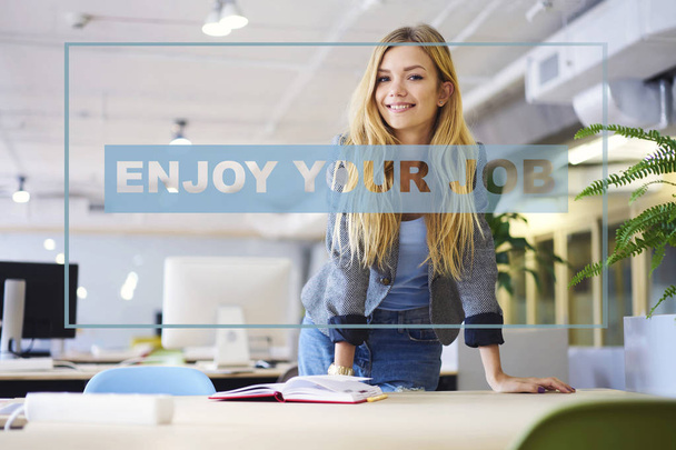 Half length portrait of positive caucasian female employee enjoying her job in coworking office. Cheerful young creative worker with blonde hair smiling at camera office, infographic conceptual idea  - Photo, image