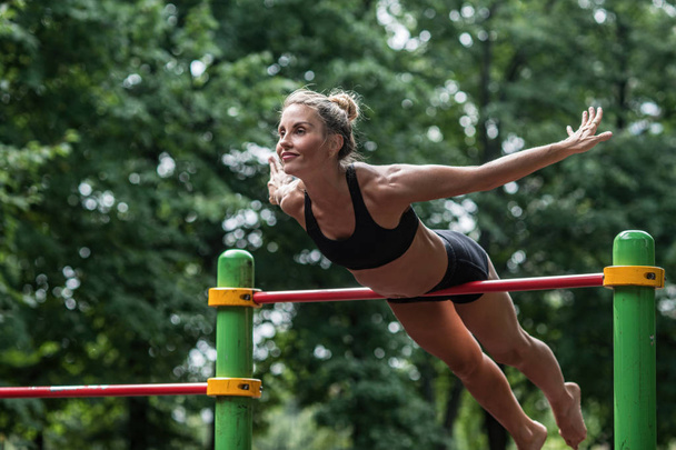 girl doing exercises on the horizontal bar in the open air. The woman is engaged in workout - Fotoğraf, Görsel