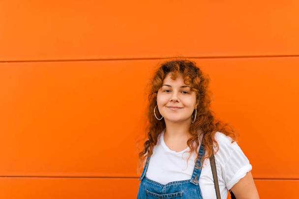 A beautiful bright girl in the style of the nineties with red hair against the background of the wall smiles happily and looks - Photo, Image