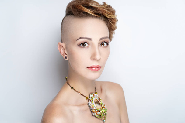 Beautiful face girl with a short haircut and a shaven temple. Elegance high fashion make-up. Ideal eye brow shape, tattoo eyebrow correction. Brown shadows glitters black arrows, persistent mascara - Foto, imagen