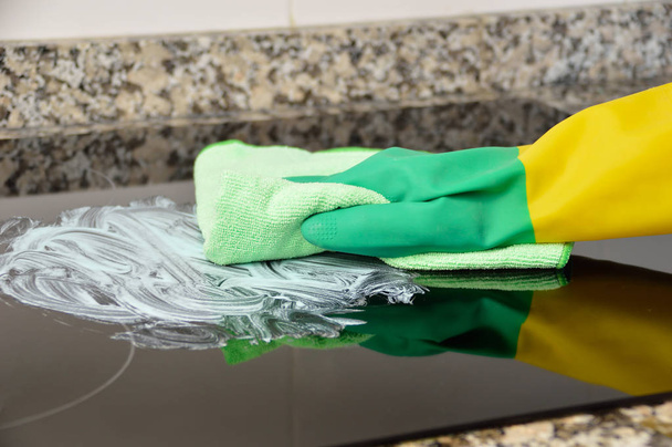 Shot of a unrecognizable person with yellow and green gloves scrubbing the surface of a oven in a kitchen - Foto, Bild