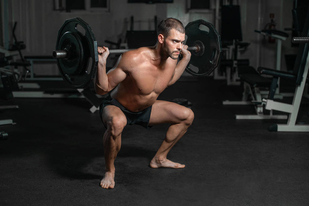 Handsome weightlifter lifting barbells with Squats. Male training with barbell, pumping legs - Fotografie, Obrázek