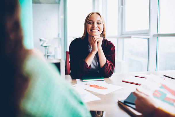 Cheerful hipster girl with blonde hair laughing during work break sitting at meeting table with sketch of design clothes.Happy student discussing successful ideas for developing own business in office - Foto, immagini