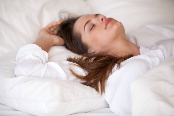 ruhige junge Frau schläft in gemütlichem weißen Bett entspannend - Foto, Bild