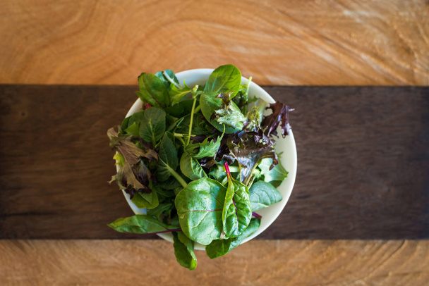 Vegetarian salad from a mix of fresh leaves in a plate on a wooden background - Zdjęcie, obraz