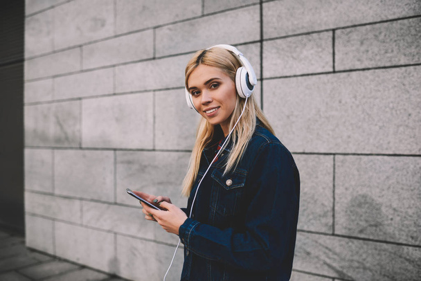 Half length portrait of positive blonde woman enjoying recreation with music while standing against promotional background.Pretty hipster girl looking at camera during listening to favorite playlist - Foto, immagini