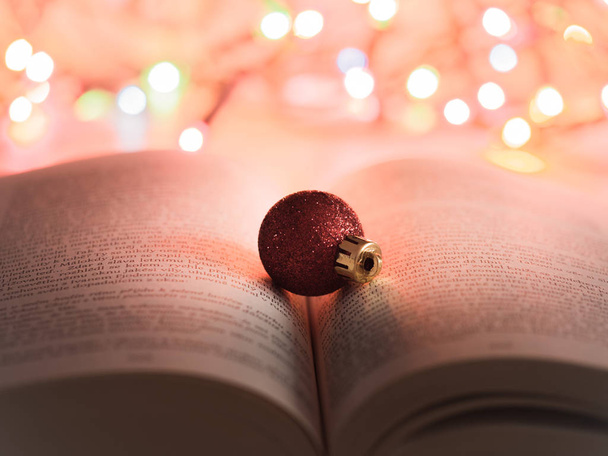 Skvělé detail červené třpytky a lesklé vánoční ornament na otevřené knihy s barevné vánoční osvětlení v pozadí - Fotografie, Obrázek