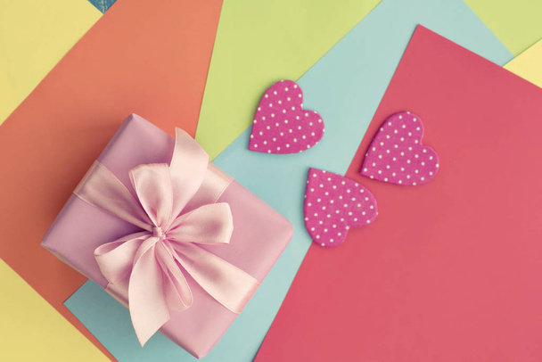 Χρωματιστά φύλλα από χαρτί διακοσμητικό καρδιά του Αγίου Βαλεντίνου δώρο πλαίσιο κορδέλα σατέν φιόγκο ροζ. Σχεδιασμός υλικού αντίγραφο χώρου - Φωτογραφία, εικόνα