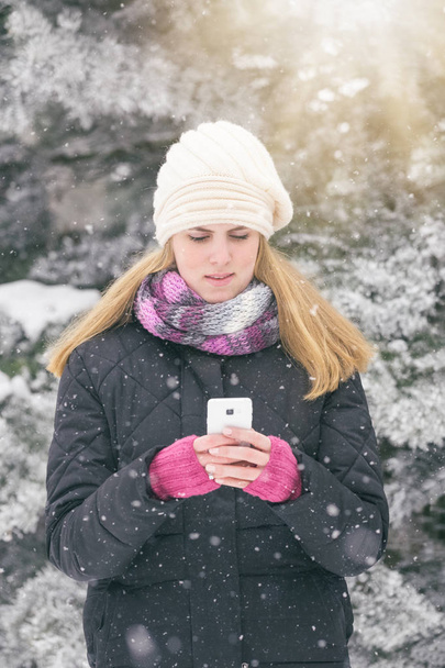 Fashionable woman holding and looking at smart phone. Winter scene. - Photo, image