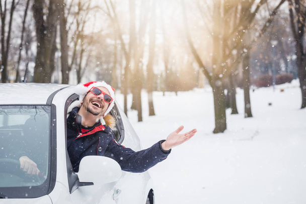 Portrait of car driver with santa hat through car window enjoying the snowy day. On the road winter vacation and holidays concept. - Photo, image