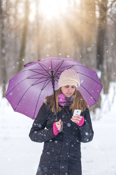 Woman with umbrella using smartphone and enjoying winter season in park. - Foto, afbeelding