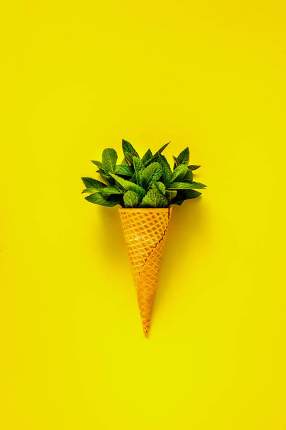 Spring or summer composition of Waffle sweet cone with fresh leaves mint on yellow background. Holiday mood concept. Flat lay, top view. - Fotografie, Obrázek