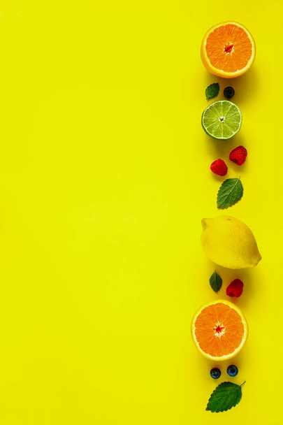 Lemon, orange, lime, raspberry, blueberry flat-lay. Creative layout made of citrus fruits and berries on yellow background. Food concept. Top view - Фото, изображение