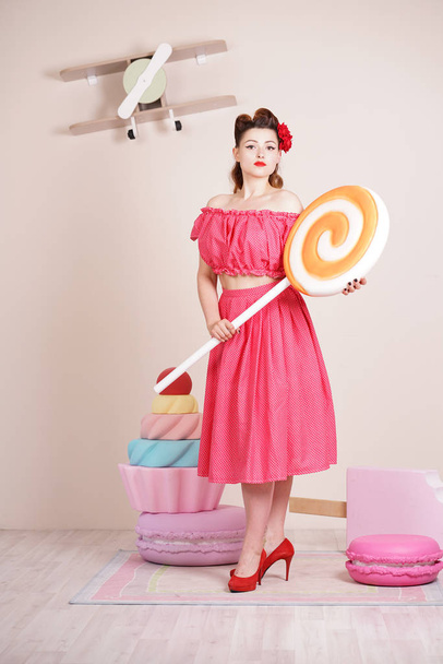 krásné elegantní pin up žena nosí červené polka dot šaty pózuje s obří sladkosti sám - Fotografie, Obrázek
