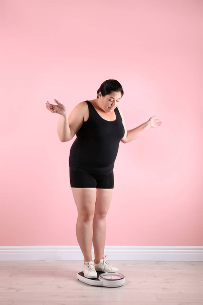 Overweight woman in sportswear using scales near color wall - Fotografie, Obrázek