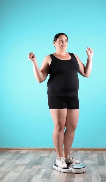 Overweight woman in sportswear using scales near color wall - Foto, imagen