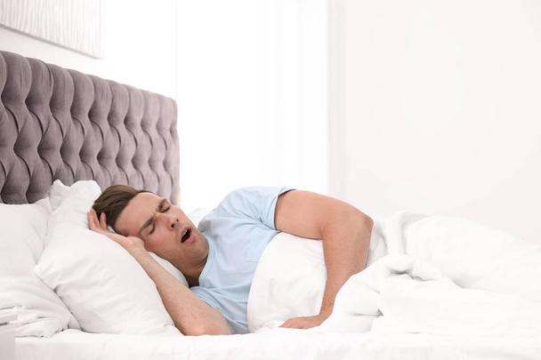Young man yawning in bed with pillows at home - Foto, Imagem