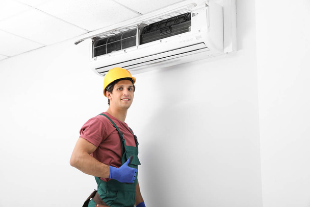 Male technician standing near air conditioner indoors - Фото, изображение
