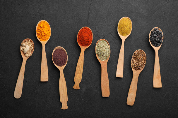 Composition with different aromatic spices in wooden spoons on dark background - 写真・画像