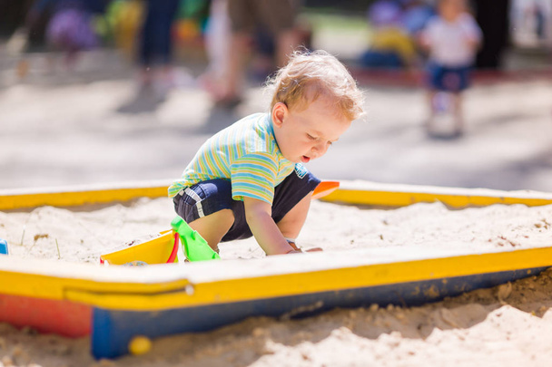 Cute baby boy playing with sand in a sandbox - Fotó, kép